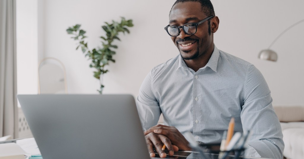 A man smiling at his laptop screen while attending a meeting.